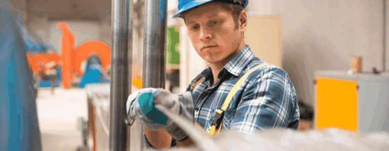 A man in a blue hat and shirt is focused on assembling a cable in a workshop setting.